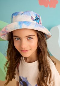 Bob en tissu tie-dye doux bleu et blanc, orné d'un imprimé coloré de personnage de dessin animé. Taille enfant avec une coupe décontractée.