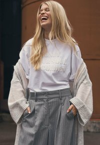 White T-shirt with embossed text, light gray cardigan, and gray pinstriped trousers. Soft textures and relaxed fit with side pockets.