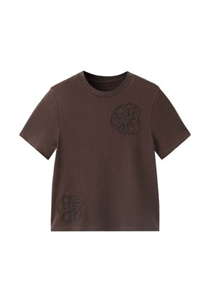 T-shirt marron à manches courtes avec col rond comportant deux motifs floraux cousus, un sur la poitrine et un près de l’ourlet inférieur.