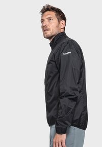 Schwarze leichte Jacke aus glattem Material mit hohem Kragen und elastischen Bündchen. Besitzt ein Logo auf der rechten Schulter.