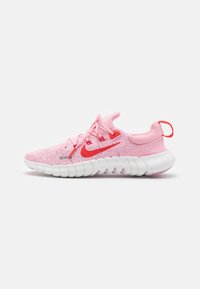 Chaussure de sport rose avec tige en maille texturée, accents rouges et semelle blanche flexible. Dispose de lacets et d'une boucle au talon pour un enfilage facile.