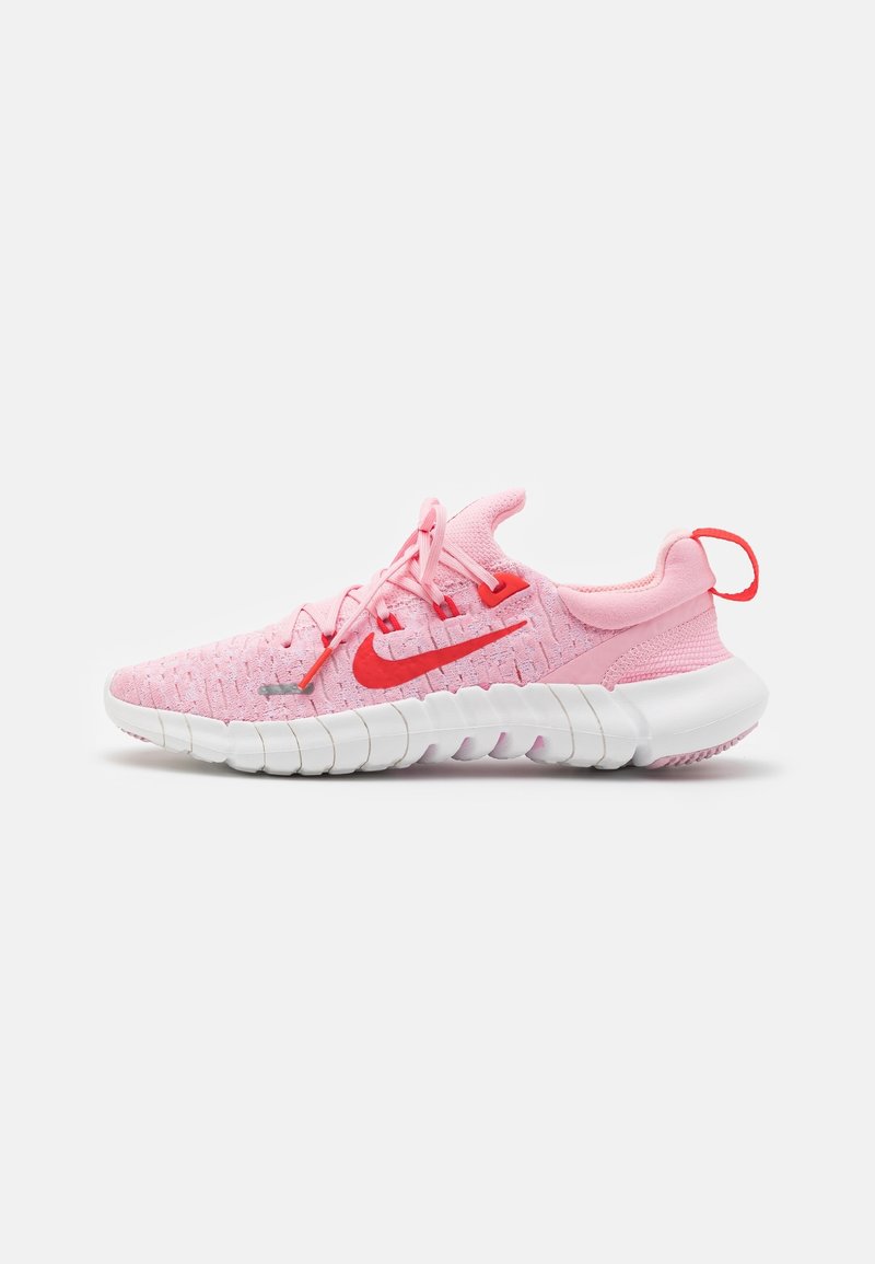 Chaussure de sport rose avec tige en maille texturée, accents rouges et semelle blanche flexible. Dispose de lacets et d'une boucle au talon pour un enfilage facile.