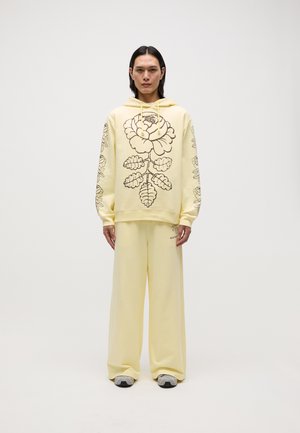 Hooded sweatshirt and loose pants in light yellow, featuring a dark floral design. Soft fabric with a relaxed fit and minimal detailing.