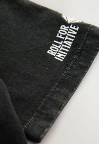 Schwarzes Baumwoll-T-Shirt mit dem Aufdruck "ROLL FOR INITIATIVE" in Weiß, einem geometrischen Akzent auf dem Ärmel und sichtbaren Nähten.