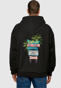 Čierna mikina s kapucňou s farebnou grafikou moteli so znakmi palmových stromov. Text znie "Kalifornský motel, Los Angeles" a "Žiadne voľné miesta."