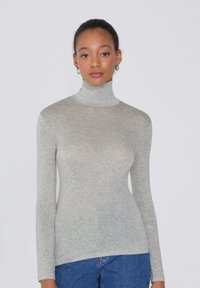 Szary, długi rękaw, górna część turtleneck wykonana z lekkiej, teksturowanej tkaniny. Posiada dopasowaną sylwetkę i subtelny blask. Noszona z niebieskimi dżinsami.