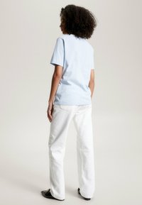 Světle modré bavlněné tričko s krátkými rukávy, v kombinaci s bílými rovnými džínami. Tento outfit má minimální detaily a volný střih.