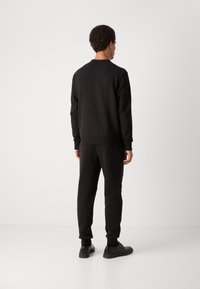 Conjunto de sweatshirt e calças de treino pretas, apresentando um corte descontraído, punhos e bainha canelados, com uma textura suave e design minimalista.