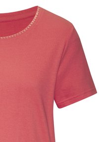 Īsa piedurkne T-krekls korallkrāsas kokvilnas audumā. Tam ir noapaļots kakla izgriezums ar dekoratīvu trīsstūra šuvju detaļu ap kaklu.