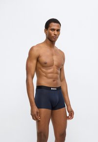 Boxer briefs bleu marine avec une ceinture noire portant un logo "BOSS" blanc. Le tissu semble lisse et ajusté, mettant en valeur un design classique.
