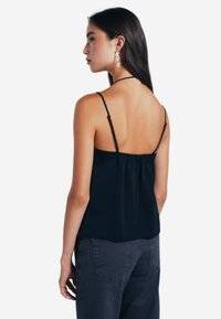 Camisola nera in satin con spalline sottili regolabili e schiena arricciata, abbinata a jeans grigio scuro. Design semplice, texture liscia.