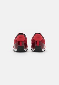 Chaussures de sport rouges avec une tige en mesh, accents noirs et semelle blanche. Présente un talon avec marque et une texture lisse.
