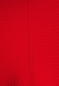 Tissu texturé rouge vif avec un motif en grille diagonale et deux coutures verticales cousues au centre.