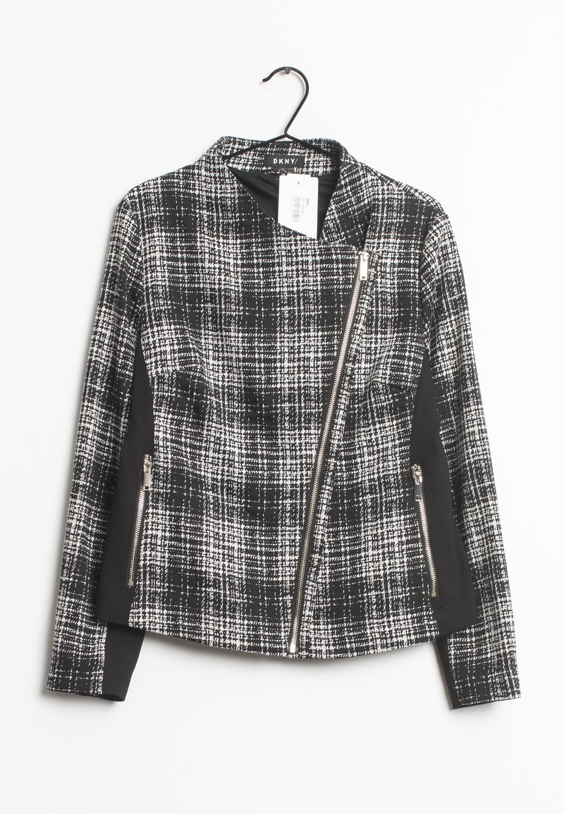 Veste pour femme à carreaux noirs et blancs avec fermeture éclair asymétrique et poches latérales zippées, suspendue sur un cintre noir.