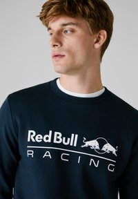 Sudadera azul marino con el logo blanco de "Red Bull Racing" y dos toros saltando. Diseño de cuello redondo y textura suave.