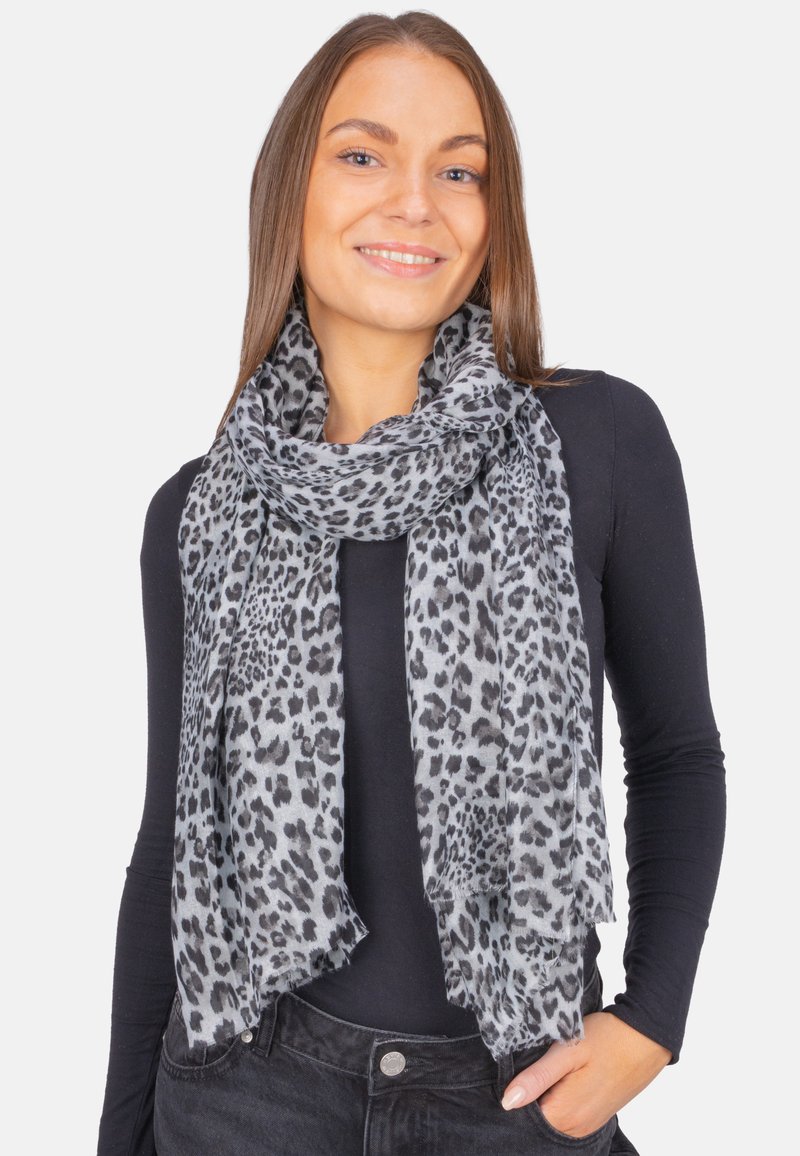 Écharpe à motif léopard gris avec une texture légère et douce, dotée d'un bord à franges. Portée lâchement autour du cou avec un haut noir.