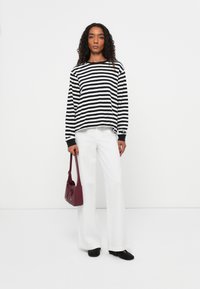 Zwart-wit gestreepte lange mouw top, witte wijde broek en een bordeaux kleurige tas. De top heeft een relaxte pasvorm en contrasterende manchetten.