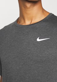 Camiseta gris de algodón con cuello redondo que presenta un logo blanco de Nike en el pecho. Textura suave y mangas cortas. Vista cercana del escote y la tela.