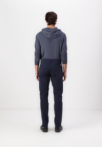 Pantaloni blu navy con una vestibilità su misura, abbinati a una felpa grigia a maniche lunghe con cappuccio regolabile, visti da dietro.