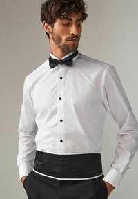 Hvid skjorte med sorte knapper og en sort satin cummerbund. Har en klassisk krave og lange ærmer med hvide manchetter.