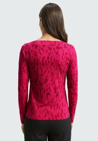 Langärmliges Oberteil in Fuchsia mit einem strukturierten abstrakten Muster in dunkleren Rottönen. Verfügt über einen breiten Ausschnitt und eine taillierte Silhouette.