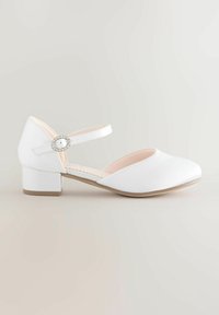 Valkoinen Mary Jane -kengät matalalla lohkarepinalla, kangas päällinen, säädettävä nilkkaremmi, jossa on strassiyksityiskohta, ja sileä pyöreä kärki.