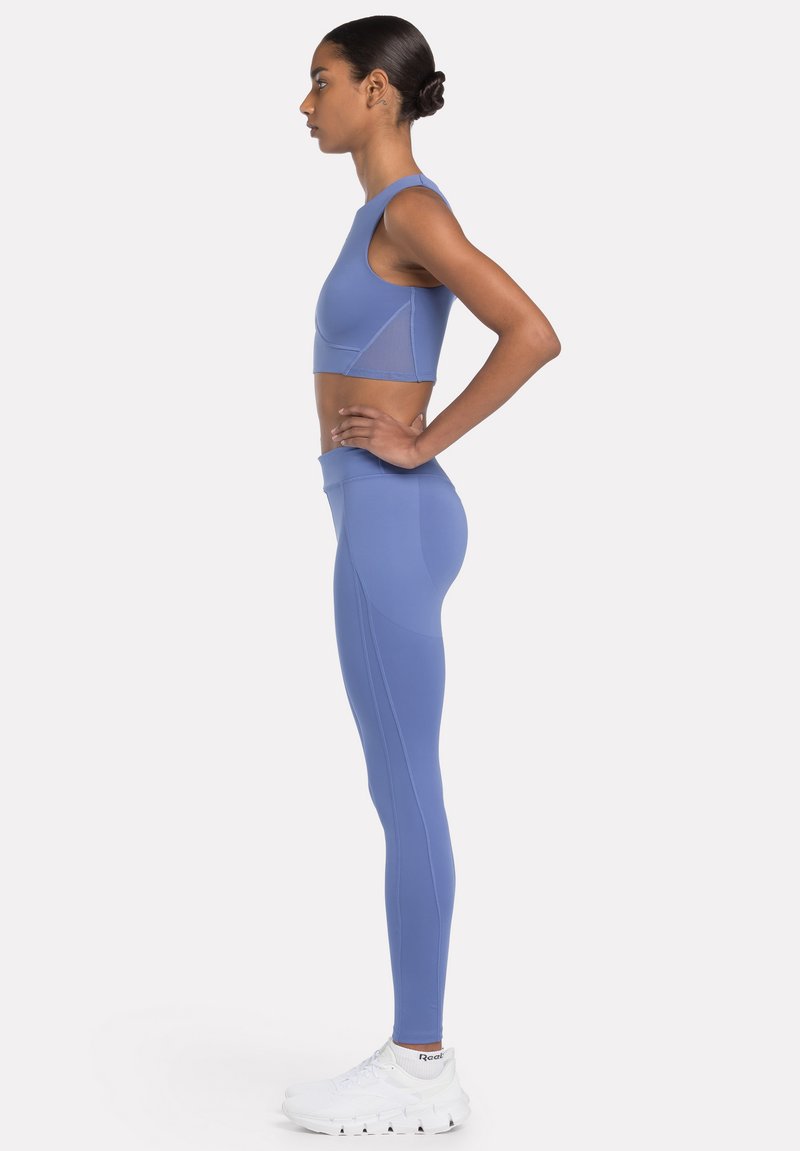 Sostén deportivo de color azul claro con escote redondeado, combinado con leggings a juego. La tela parece suave, con costuras mínimas y un ajuste elegante.