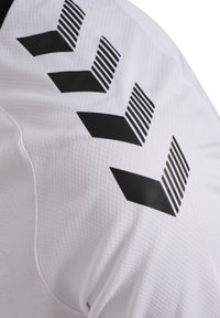 Biała sportowa koszulka z czarnymi wzorami w zygzak i paskami na ramionach, wykonana z teksturowanej, oddychającej tkaniny.