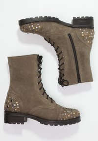 Khaki semišové kotníkové boty s kulatou špičkou, šněrováním vpředu, bočním zipem a cvočkovými akcenty na patě a špičce. Černá gumová podešev.