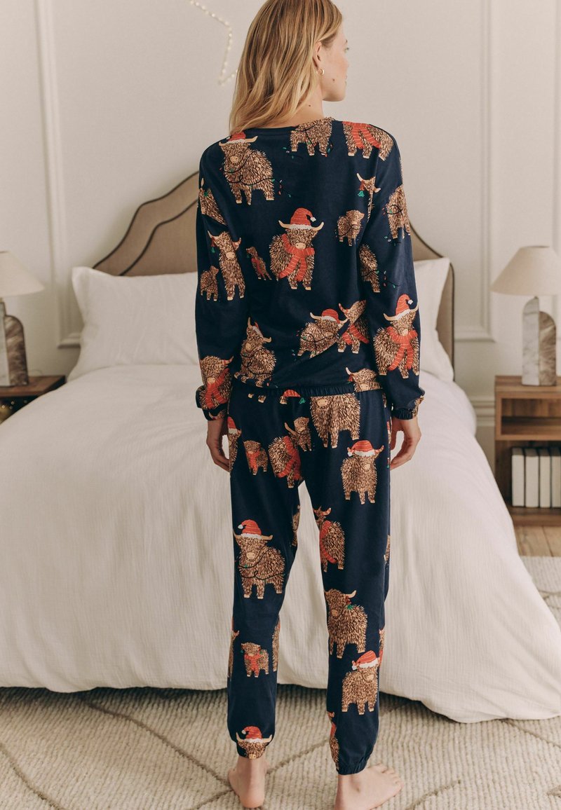 Marinblå pyjamasset tillverkat av mjukt tyg, med ett upprepat mönster av tecknade björnar som bär jultomteluvor och sjalar, elastisk midja.