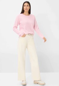 Rosa gestrickter Pullover mit Rundhalsausschnitt und langen Ärmeln, kombiniert mit cremefarbenen weit geschnittenen Hosen und cremefarbenen Schuhen mit dicker Sohle.