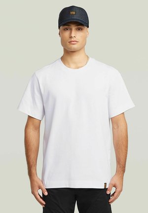 Hvid bomulds t-shirt med korte ærmer, rund hals og en afslappet pasform. Sammen med en mørk denim baseball cap med et logo patch.