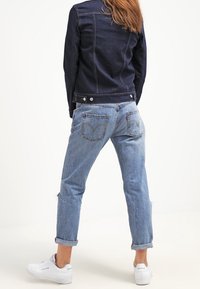 Ciemnogranatowa kurtka dżinsowa o dopasowanym kroju, w zestawieniu z jasnoniebieskimi, lekko zniszczonymi spodniami o prostym kroju. Białe sneakersy dopełniają stylizację.