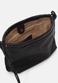 Sac bandoulière en cuir noir avec intérieur en tissu beige, fermeture à pression magnétique et poche intérieure zippée.
