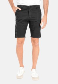 Pantaloni corti neri da uomo in misto cotone, con un design classico, passanti per cintura, chiusura con zip e tasche laterali. Indossati con sneaker bianche.