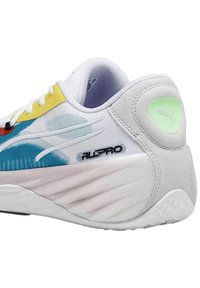 Baskets Puma avec une tige en mesh blanc, des accents colorés en jaune, bleu et rouge, dotées d'une semelle intermédiaire texturée et d'un logo vert doux.