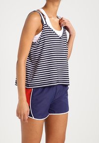 Canotta a strisce blu navy e bianche con scollatura a V, abbinata a pantaloni corti blu navy con un pannello laterale rosso e bordo bianco.