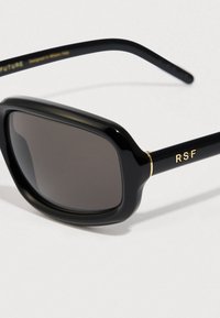 Storebriller med mørke, tonede linser, en blank overflade og guldaccenter på stellet. RSF-logo på siden.