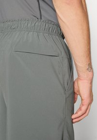 Calções atléticos cinzentos com um cós elástico, bolsos laterais e logótipo "Dri-Fit". Textura do tecido suave e design leve.