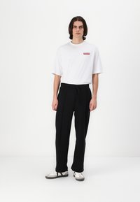 White short-sleeve t-shirt with a red text graphic, paired with black loose-fit pants and white sneakers with black accents.
