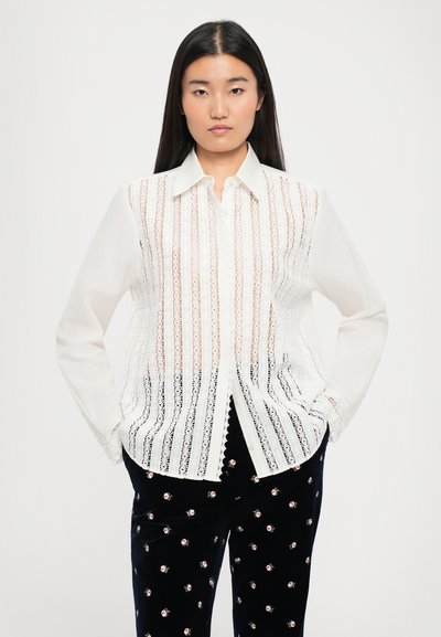 Balta mežģīņu blūze ar vertikālām svītrām, pogājamais priekšpuse un garās piedurknes, kombinēta ar melniem samta biksēm ar ziedu rakstu.