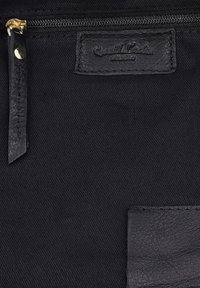 Black fabric bag section with a small zippered pocket and two stitched leather labels, one embossed with partially visible text.