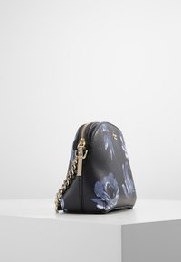 Černá květinová kabelka s texturovaným povrchem; obsahuje zlatý řetízkový popruh, zipové zavírání a velké modré květinové vzory na jedné straně.