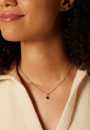 Zilveren ketting met een ronde, diep rode hanger. De hanger heeft een gladde oppervlakte en hangt aan een delicate ketting.