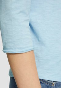 Haut en coton bleu clair ajusté avec des manches à longueur de coude ; texture douce ; poignets roulés ; design uni, porté avec du denim.