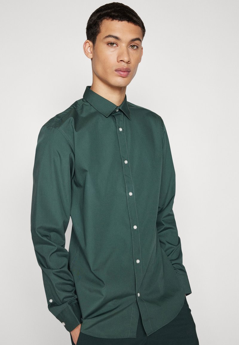 Ciemnozielona koszula z długim rękawem, z kołnierzykiem zapinanym na guziki i z przodem z plisą, wykonana z gładkiego materiału, z białymi guzikami i dopasowanym krojem.