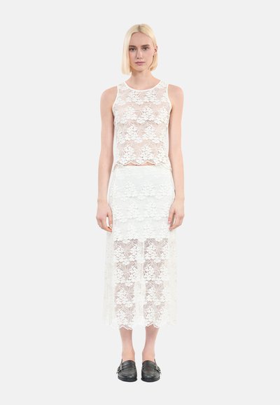 Haut en dentelle blanche à encolure ronde et coupe courte, assorti à une jupe maxi en dentelle blanche avec des designs superposés et une texture transparente.