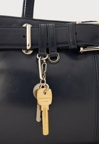 Navy leather handbag with shiny silver hardware, featuring a detachable keychain with one gold key and a silver key on a metal ring.