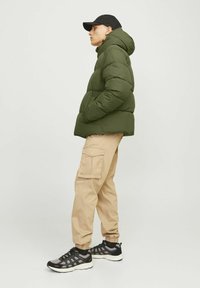 Grøn pufferjakke med hætte, beige cargo-bukser og sorte sportsko. Egenskaber inkluderer en rund bund og tekstureret stof.