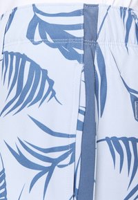 Primer plano de una tela azul clara con un estampado de hojas tropicales en azul oscuro y una costura de bolsillo.